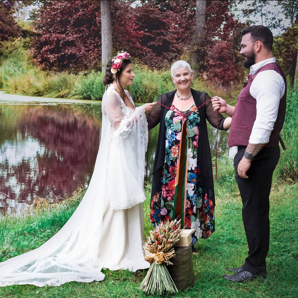 A woman with another woman and man during their ceremony in front of the lake